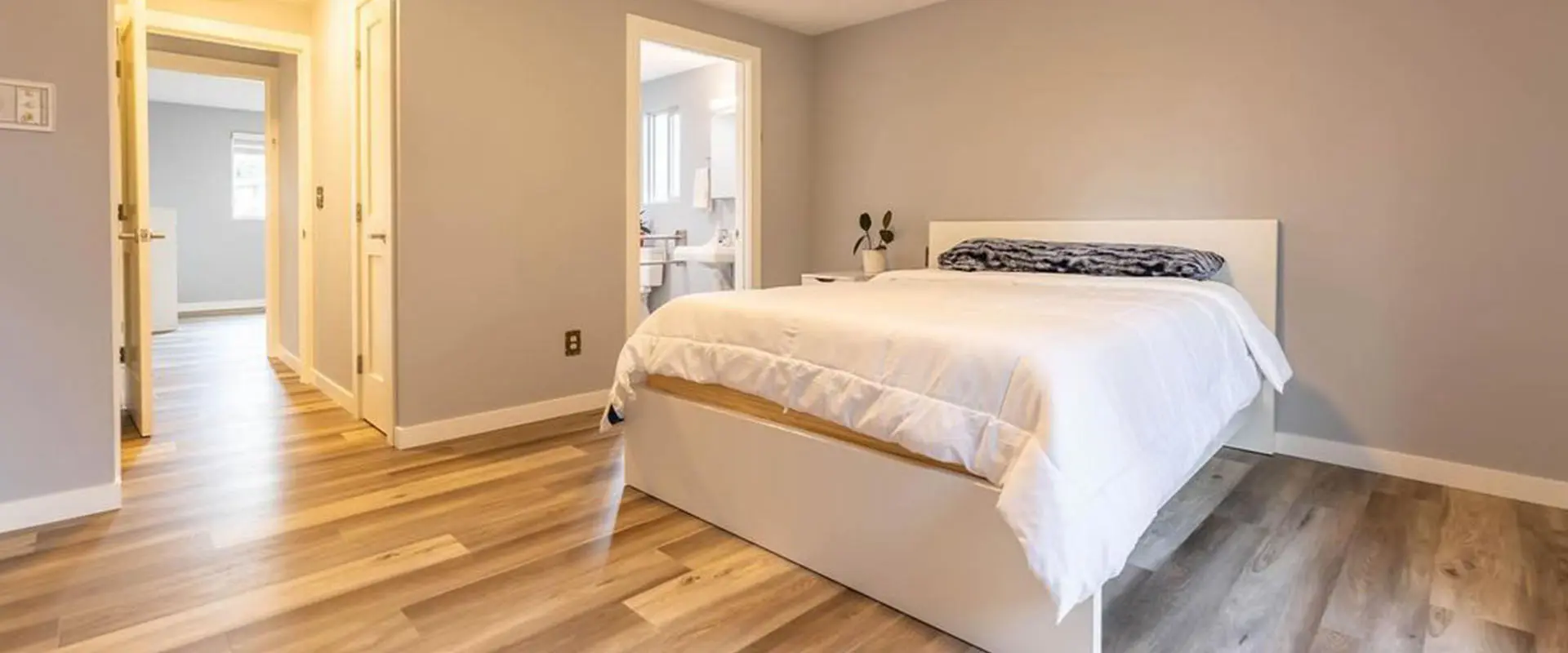 A bedroom with hard wood floors and white walls.